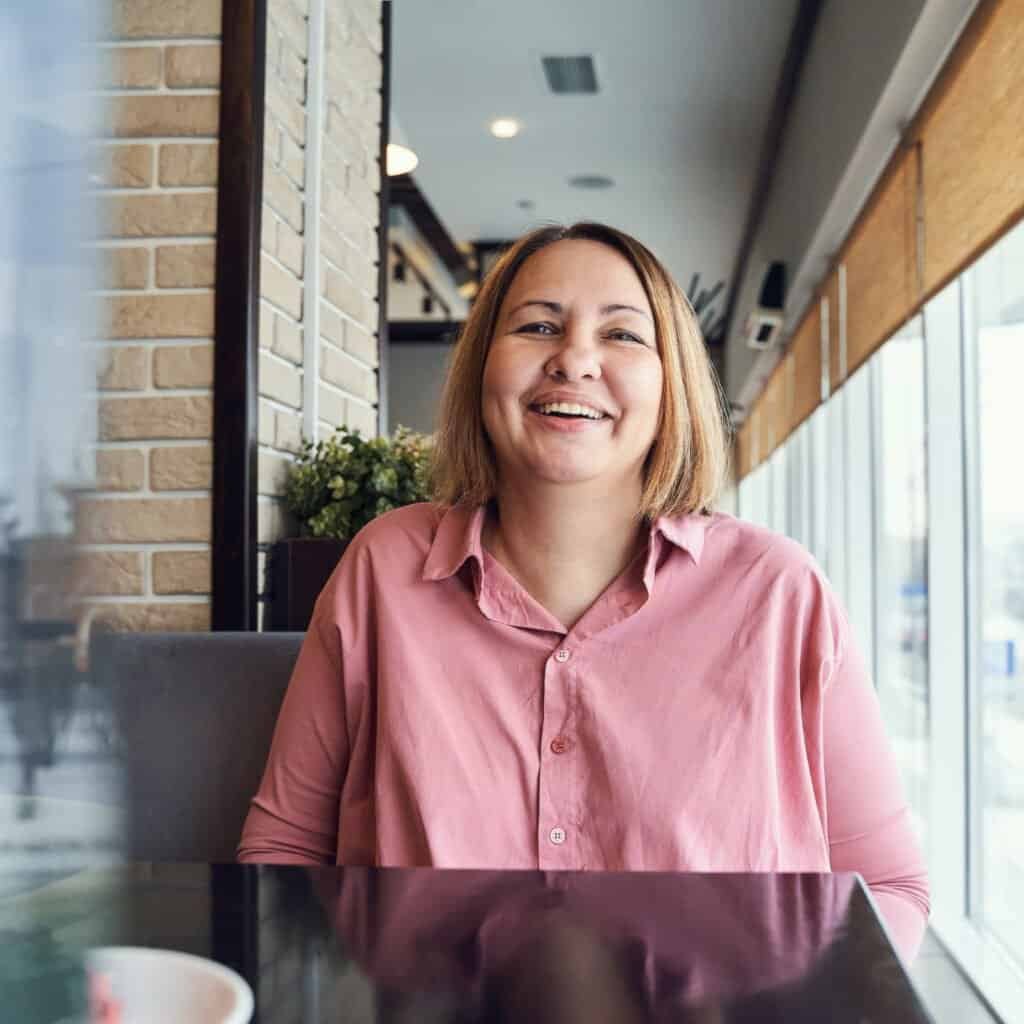 Woman smiling in cafe with Tahoe Art Tile decor, warm natural light, and modern interior.